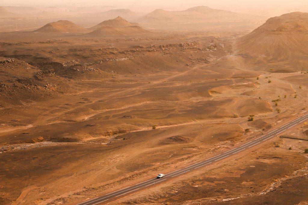 Une voiture de location élégante sur une route panoramique au Maroc avec un paysage désertique en arrière-plan